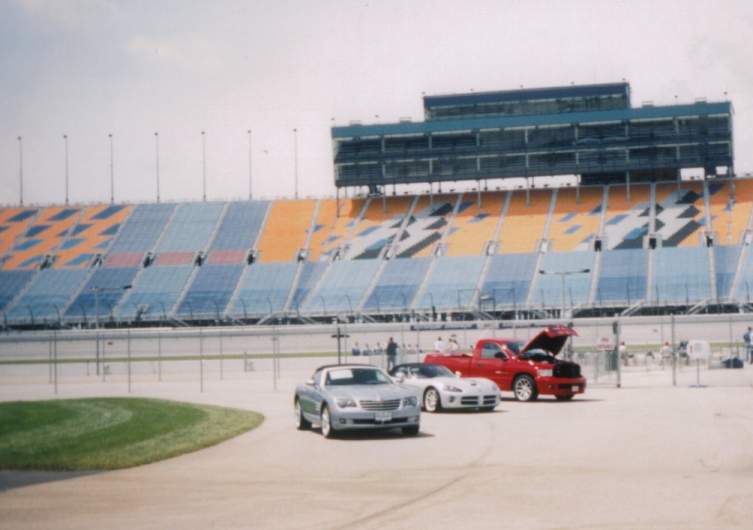 Silver convertible, white sports car, and red pickup truck parked in front of stadium seating