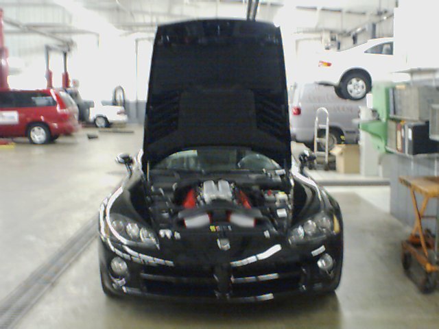 Black Dodge Viper with hood open, showing engine. Other vehicles in background of garage