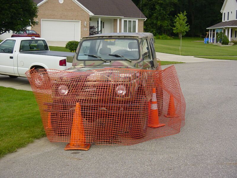 Camouflaged off-road vehicle behind orange safety netting and traffic cones