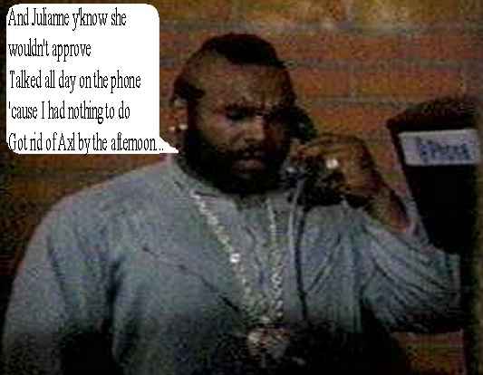 Man with mohawk and beard on phone, wearing a grey shirt and gold chains