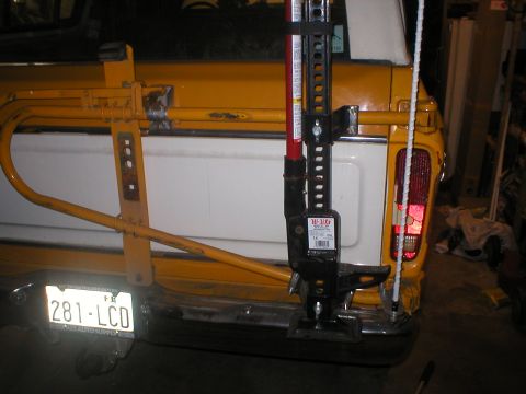 1978 Ford Bronco - A Hi-Lift jack is mounted to the rear bumper and spare tire carrier of a yellow vehicle.