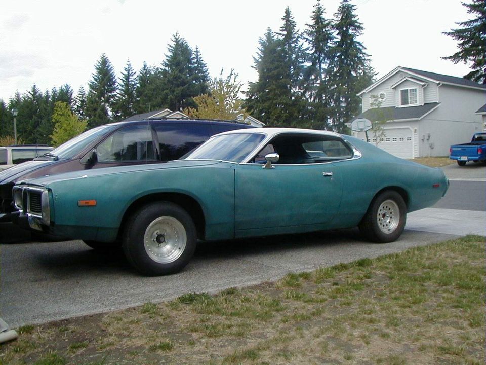Teal coupe with a white roof, parked on a driveway next to a dark van