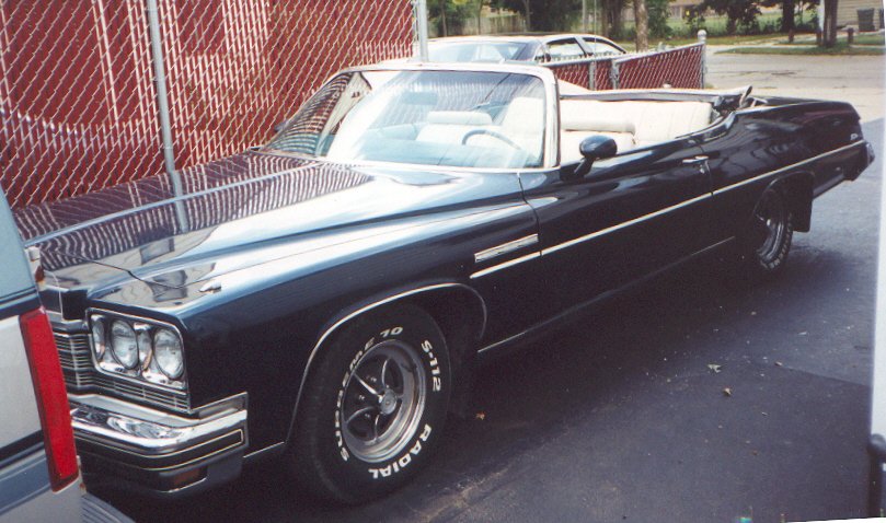 dark blue convertible parked next to a fence, another car is visible in the background