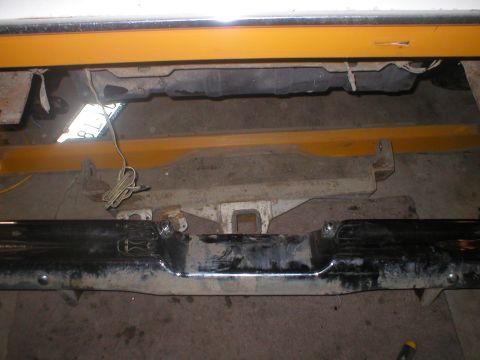 1978 Ford Bronco - The underside of a vehicle shows a chrome rear bumper and frame components, with yellow support bars overhead.