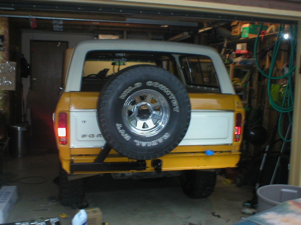 Yellow and white Ford Bronco, rear view, spare tire on tailgate, in garage