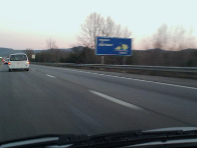 White van on highway, rear view. Blue highway sign in background