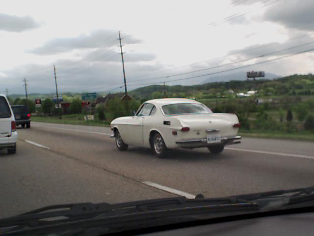 White Volvo P1800 coupe from rear, driving on highway