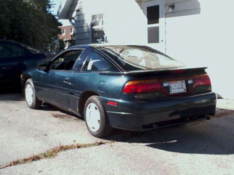 1994 Eagle Talon - A dark green coupe is parked outside a building with a dark blue car partially visible to the left.
