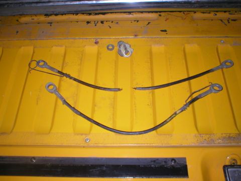 1978 Ford Bronco - Broken tailgate cables are laid out on a yellow surface, possibly a truck bed.