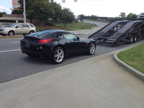 1995 Ford Bronco - A black Pontiac Solstice GXP Coupe is seen from the rear 3/4 angle as it is loaded onto a car hauler.