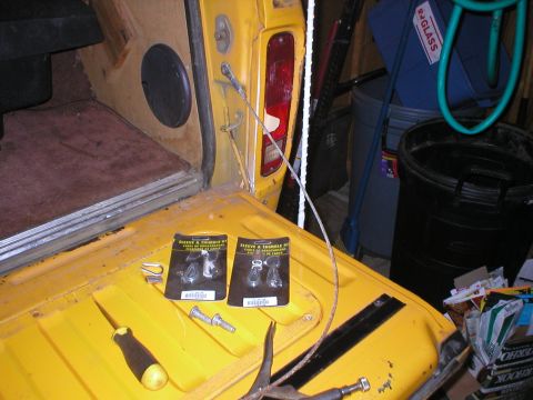 1978 Ford Bronco - Two packages of tailgate cables are laid out on a yellow surface next to a screwdriver and bolts.