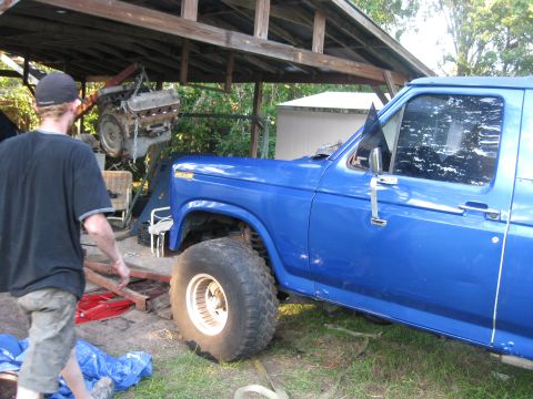 1994 Ford Bronco - Blue Ford truck undergoing engine removal, parked under a wooden shelter.