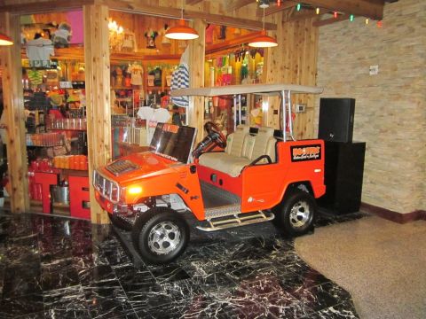 1991 Ford LTD Crown Victoria - This orange golf cart, resembling an H2 Hummer, is branded with Hooters logos and displayed indoors.
