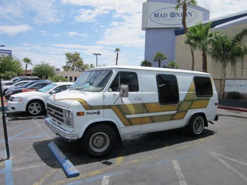 1991 Ford LTD Crown Victoria - A white Chevrolet van with distinctive gold and brown side graphics is parked in a lot under a bright sky.