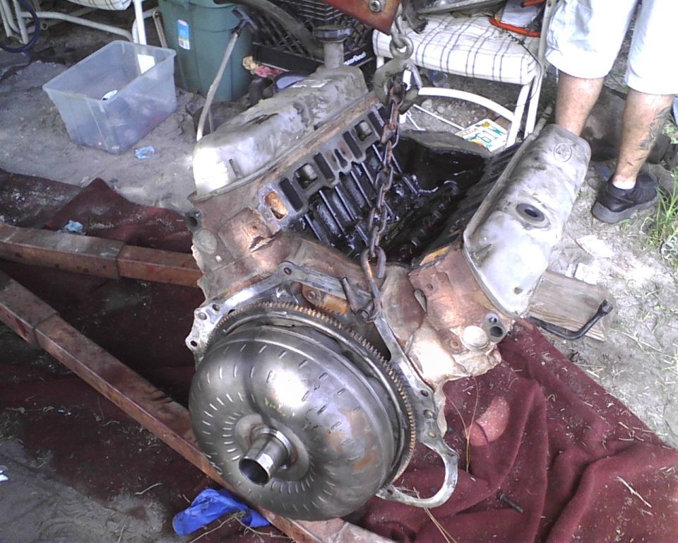 Engine and torque converter assembly suspended by chains, resting on a red cloth and wooden beams