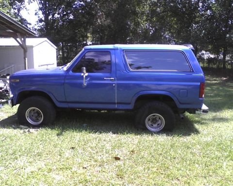 1985 Ford Bronco - Side view of a blue Ford Bronco with tinted windows and aftermarket wheels.