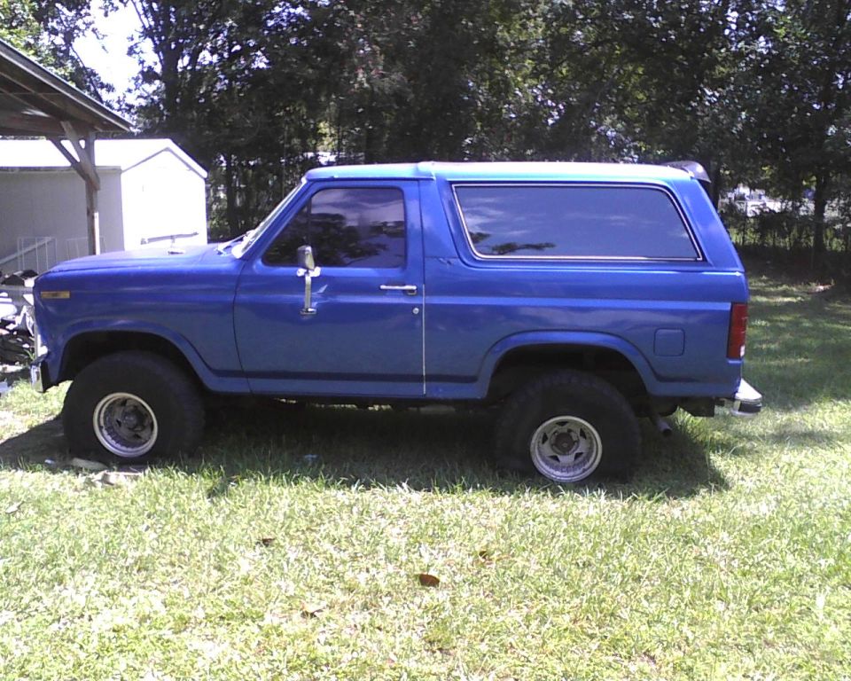 Blue Ford Bronco with aftermarket wheels parked on grass