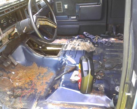 1985 Ford Bronco - The interior of a 1985 Ford Bronco reveals significant rust on the floor, along with the steering wheel and dashboard components.