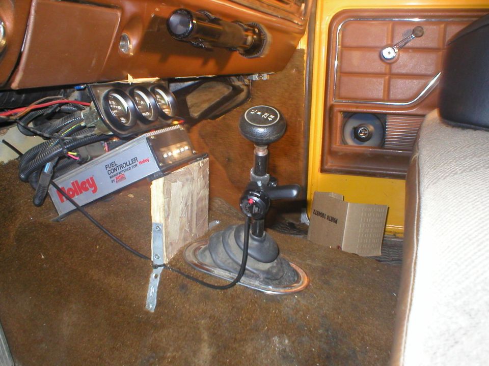 Interior shot of a vehicle showing a shifter, Holley fuel controller, and gauges. The door panel and seat are visible