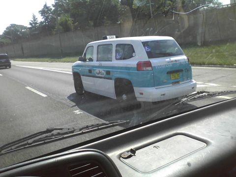 2003 Ford Crown Victoria - A white and blue taxi van, marked 'FLASH CAB', is seen from behind on the highway, displaying a disabled access symbol.