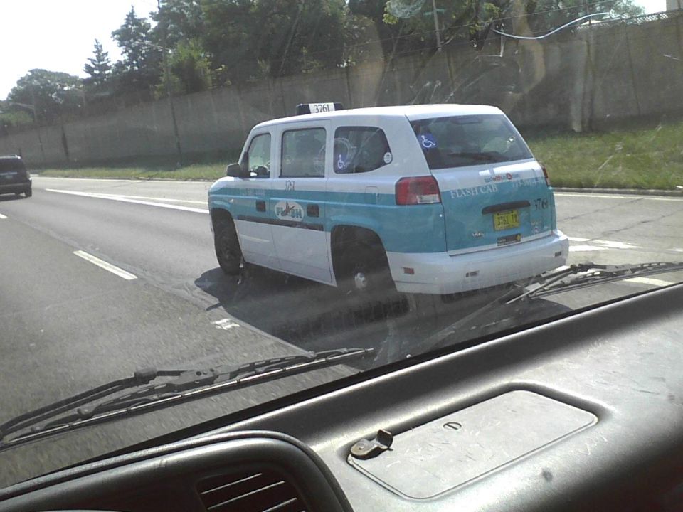 Rear view of a white and blue taxi van with a disabled symbol and 'FLASH CAB' text