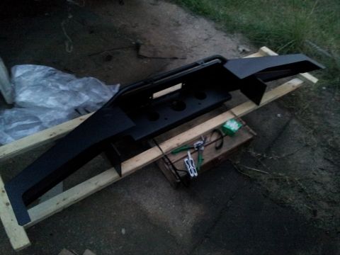 1986 Ford Bronco - A black aftermarket bumper with a winch cutout is shown resting on wooden beams outdoors.
