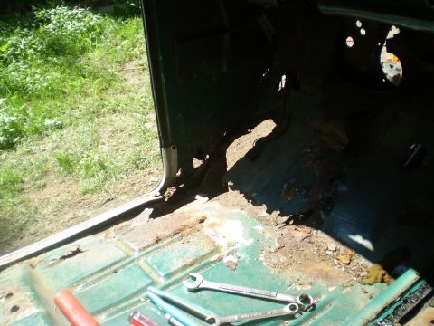 1979 Ford Bronco - The interior of a vehicle shows extensive rust damage on the floor and lower body panels, with tools laid out for repair.