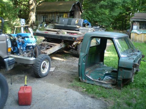 1979 Ford Bronco - A green truck cab sits on grass next to a chassis with a blue engine, suggesting a project vehicle.