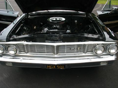1964 Ford Galaxie - The front grille and headlights of a classic black Ford Galaxie are visible, with the hood open to reveal the engine.