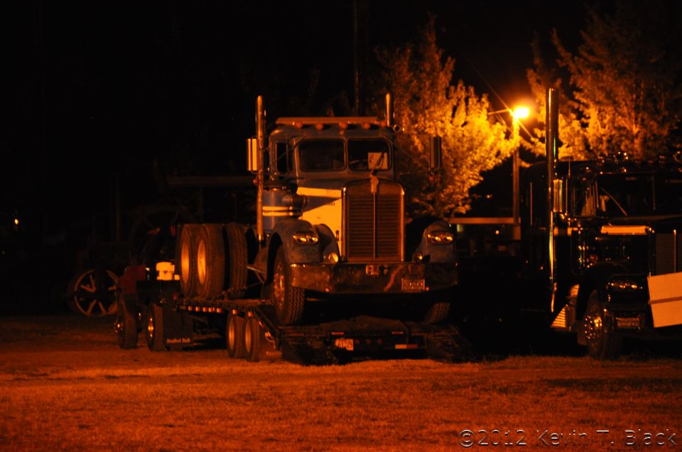 Truck on a trailer at night, another truck to the right