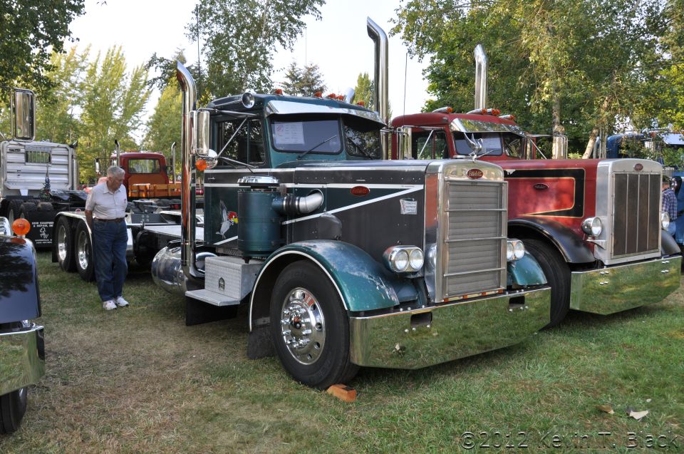 Two semi-trucks parked on grass, one dark green and black, the other red and black