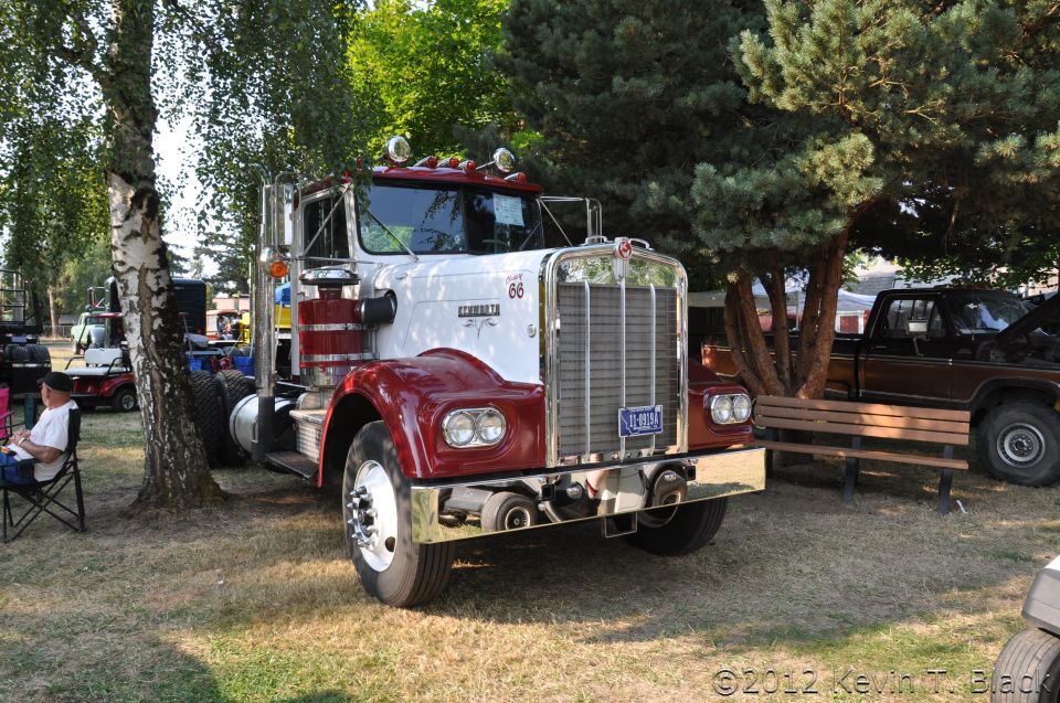 White and red 1959 Kenworth W900A truck parked on grass, front 3/4 view