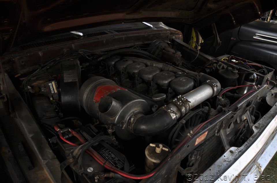 Engine bay with a large inline-six diesel engine, air intake, and battery. Brown hood is open