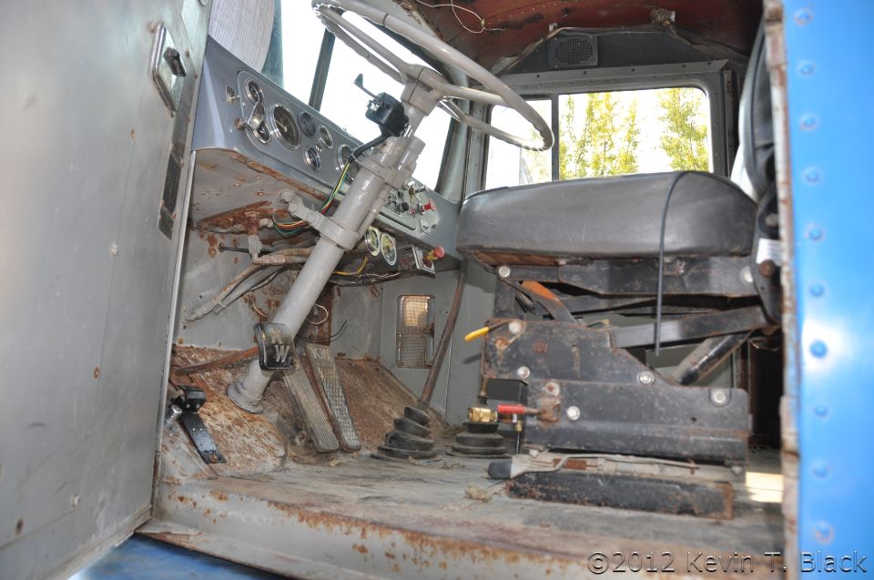 Interior view of a rusty truck cab, showing the dashboard, steering wheel, and seats