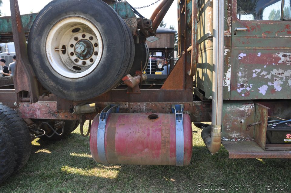 Side view of a rusty truck with a large red fuel tank and spare tire
