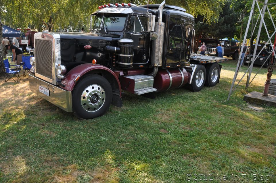 Black Peterbilt 379 semi-truck with maroon fenders and fuel tanks parked on grass