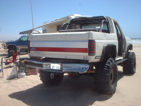 1991 Ford Bronco - This modified Ford Bronco is parked on a sandy beach with a blue truck in the background.