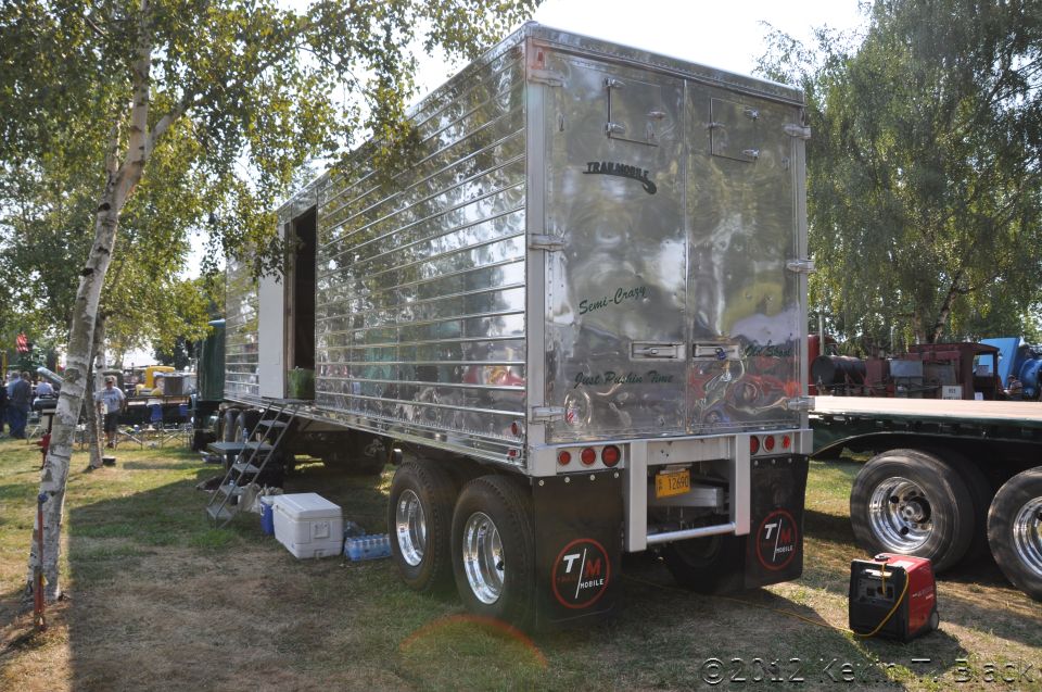 Rear view of a shiny chrome trailer with 'TRAIL MOBILE' and 'Semi-Crazy' graphics; a flatbed trailer is to the right