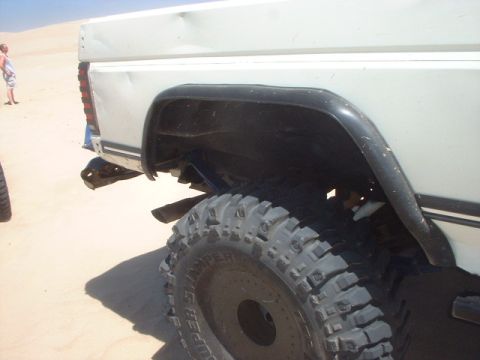 1991 Ford Bronco - A white SUV with significant body damage sits on a sandy terrain, its rear tire and fender flare prominently displayed.