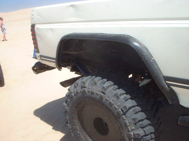 White lifted truck rear quarter with black fender flare and large Super Swamper tire on desert sand