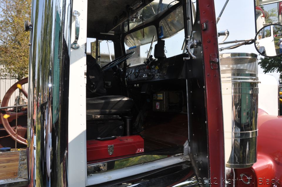 view inside a truck cab, showing dashboard, steering wheel, seat, and a red toolbox. A large chrome exhaust stack is visible outside