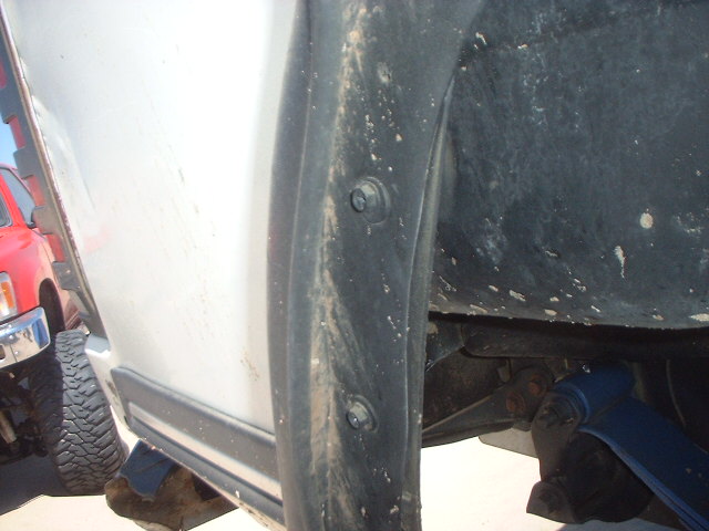Silver vehicle rocker panel and black fender flare with bolts, muddy, suspension visible behind