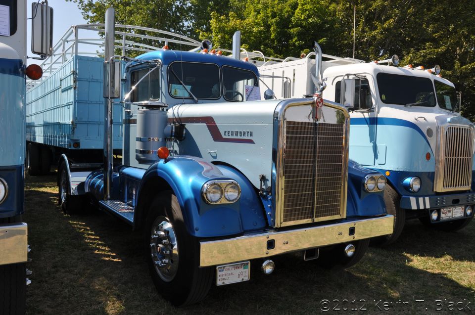 Blue and white Kenworth truck with a trailer, parked next to another truck