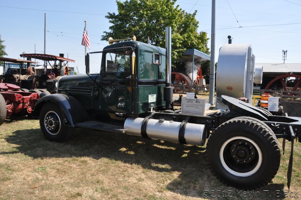 Green semi-truck cab with a silver fuel tank and large exhaust stack, parked on grass