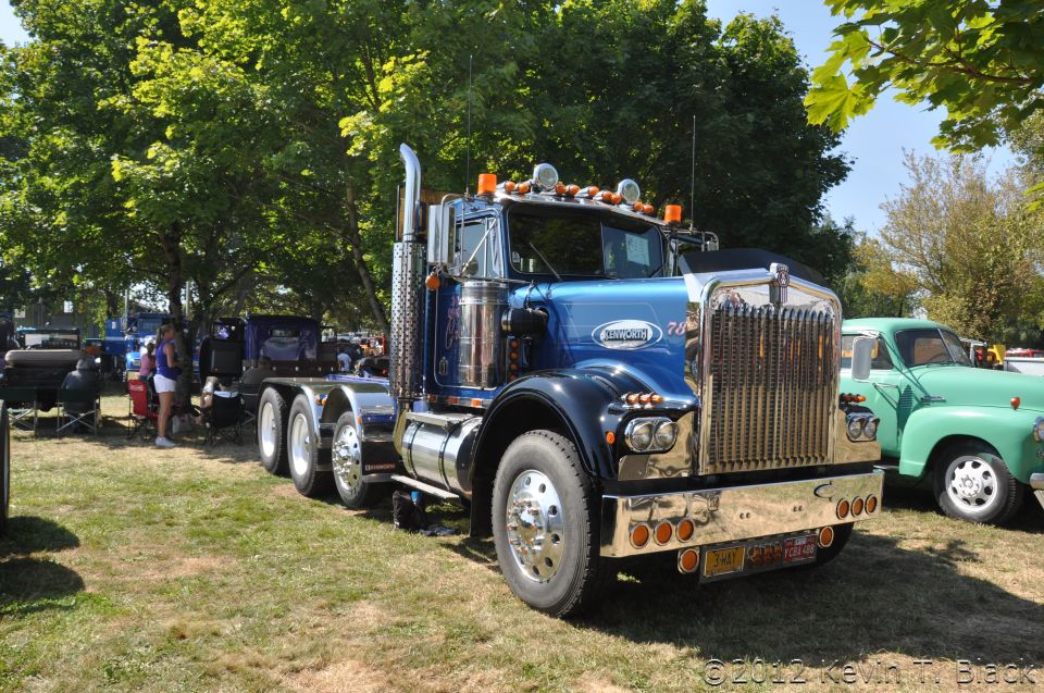 Blue Kenworth W900A semi-truck parked on grass, with a green vintage truck to its right