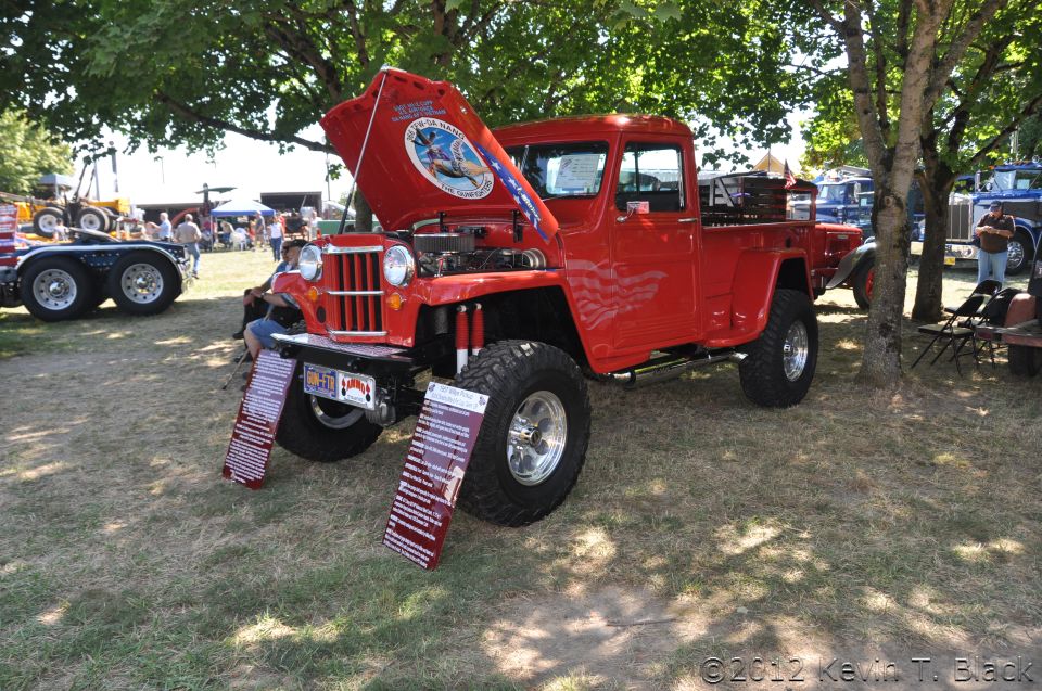 red pickup truck with hood open, showing engine, parked on grass at an outdoor event