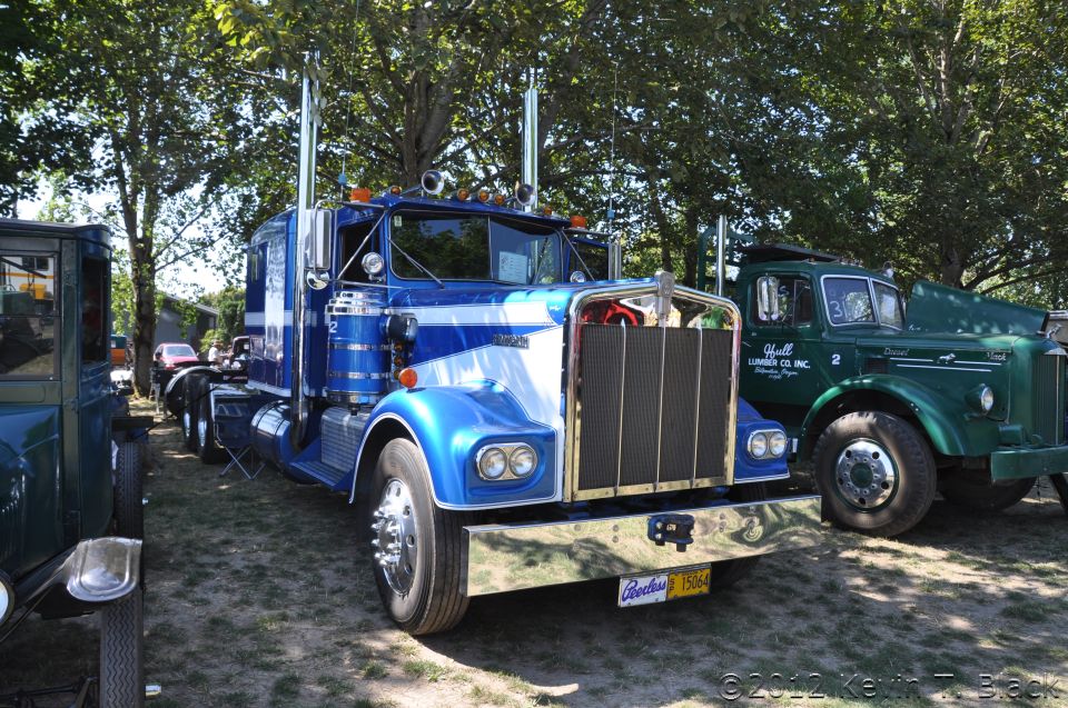 Blue semi-truck with chrome grille and stacks, parked next to a green truck