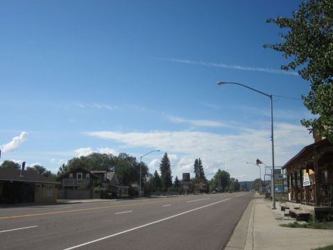 1991 Ford LTD Crown Victoria - A view down a road lined with buildings and trees on a clear day.