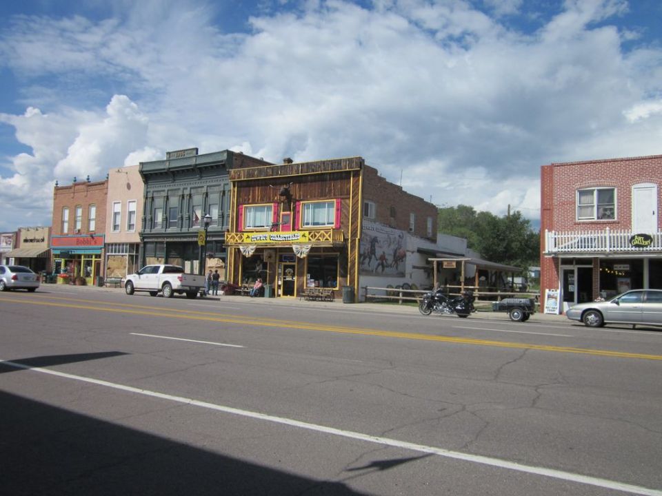 Street view of buildings with a white pickup truck, a motorcycle with trailer, and a silver sedan parked