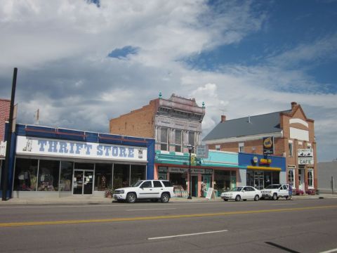 1991 Ford LTD Crown Victoria - A row of storefronts lines a street under a partly cloudy sky, with several vehicles parked in front.